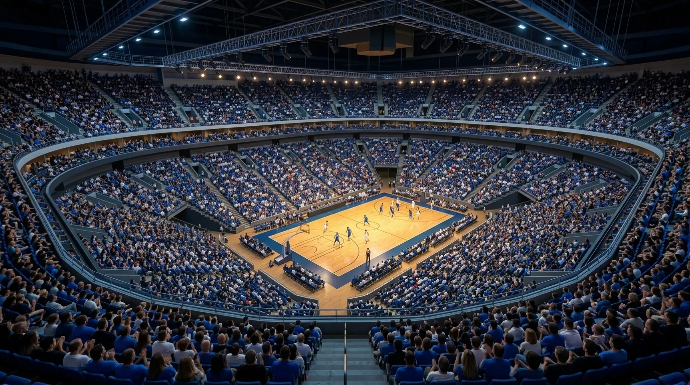 Arena de basquete lotada, vista da arquibancada superior atrás da cesta, com um jogo em andamento na quadra iluminada